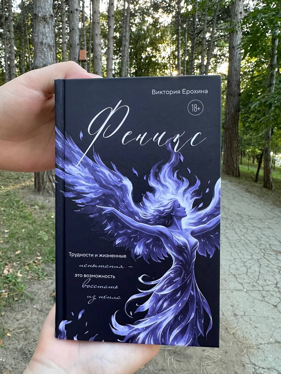Книга «Феникс» Виктории Ерохиной в руках: на обложке женщина-феникс с крыльями из света